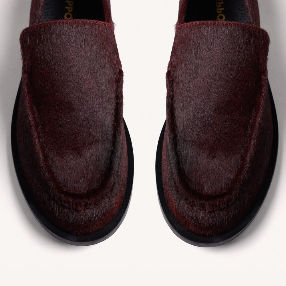A pair of Gioseppo dark burgundy slip-on loafers with a textured hair-on-hide finish, displayed on a clean off-white background.