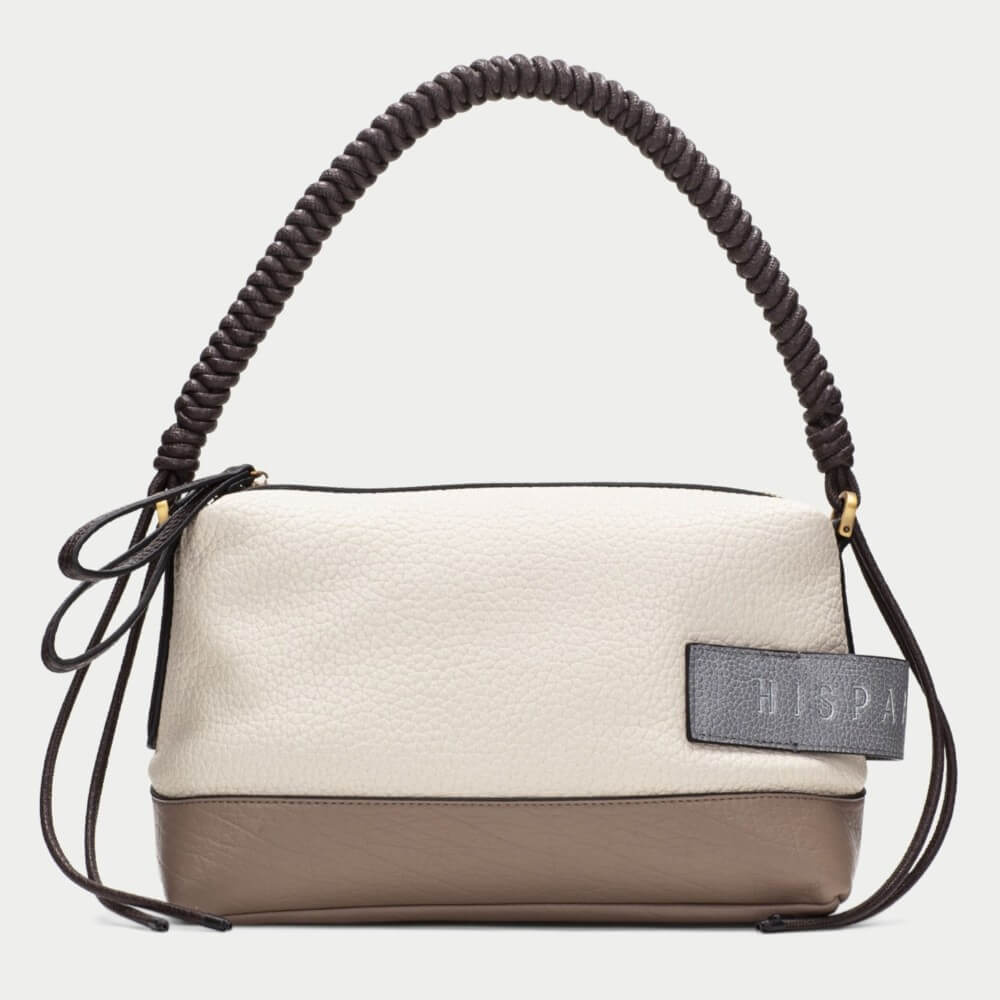 A colour-blocked handbag with a textured off-white top half, a taupe-brown bottom half, and a dark brown coiled shoulder strap. A dark grey leather patch on the front features the brand name 'HISPANITAS' in gold lettering.