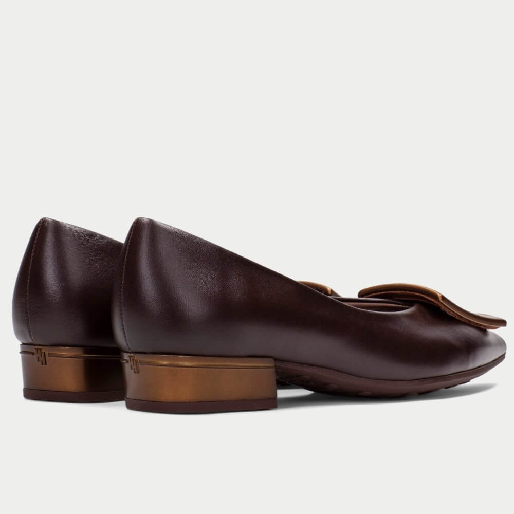 A pair of Hispanitas dark brown leather flat shoes with low block heels and a decorative brown leather bow detail on the toe, shown from a side-rear angle against a light grey background.