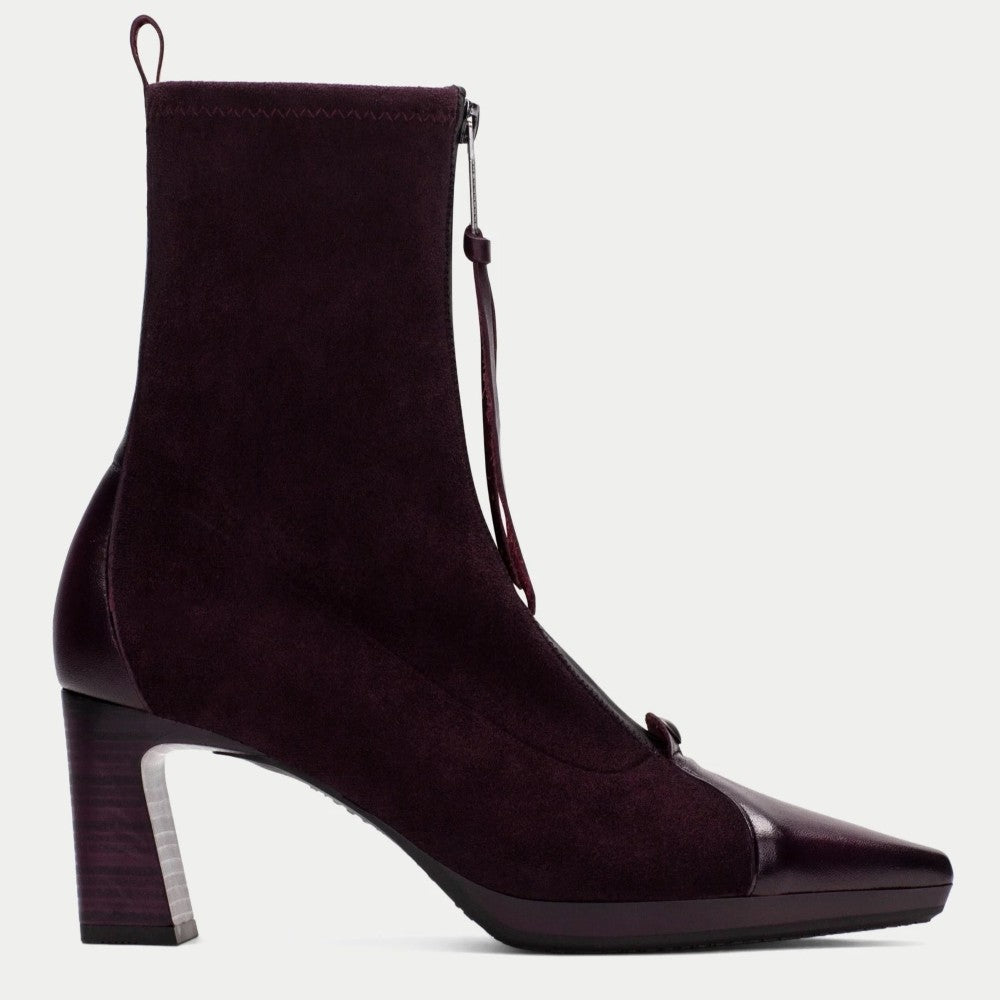 A Hispanitas dark plum purple ankle boot with a suede-like upper, a pointed toe with a glossy finish, and a chunky block heel, shown against a plain light gray background.