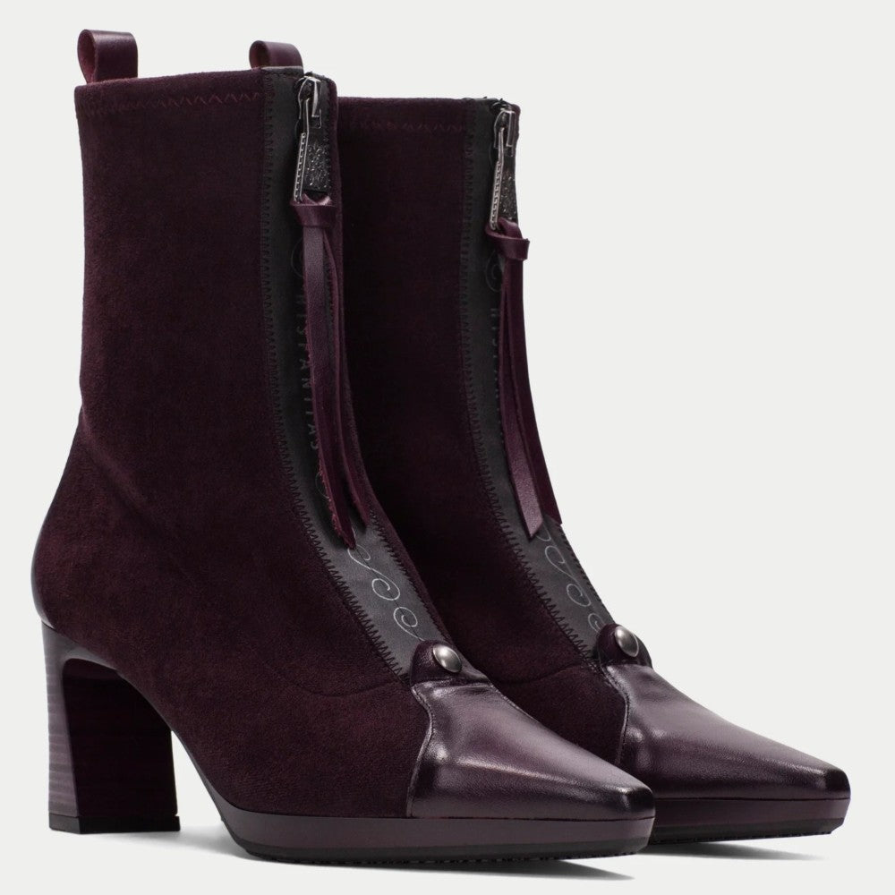A pair of Hispanitas dark plum purple ankle boots with a mix of suede and smooth leather panels, featuring a block heel, pointed toe, and side zippers with pull tabs, shown against a light gray background.