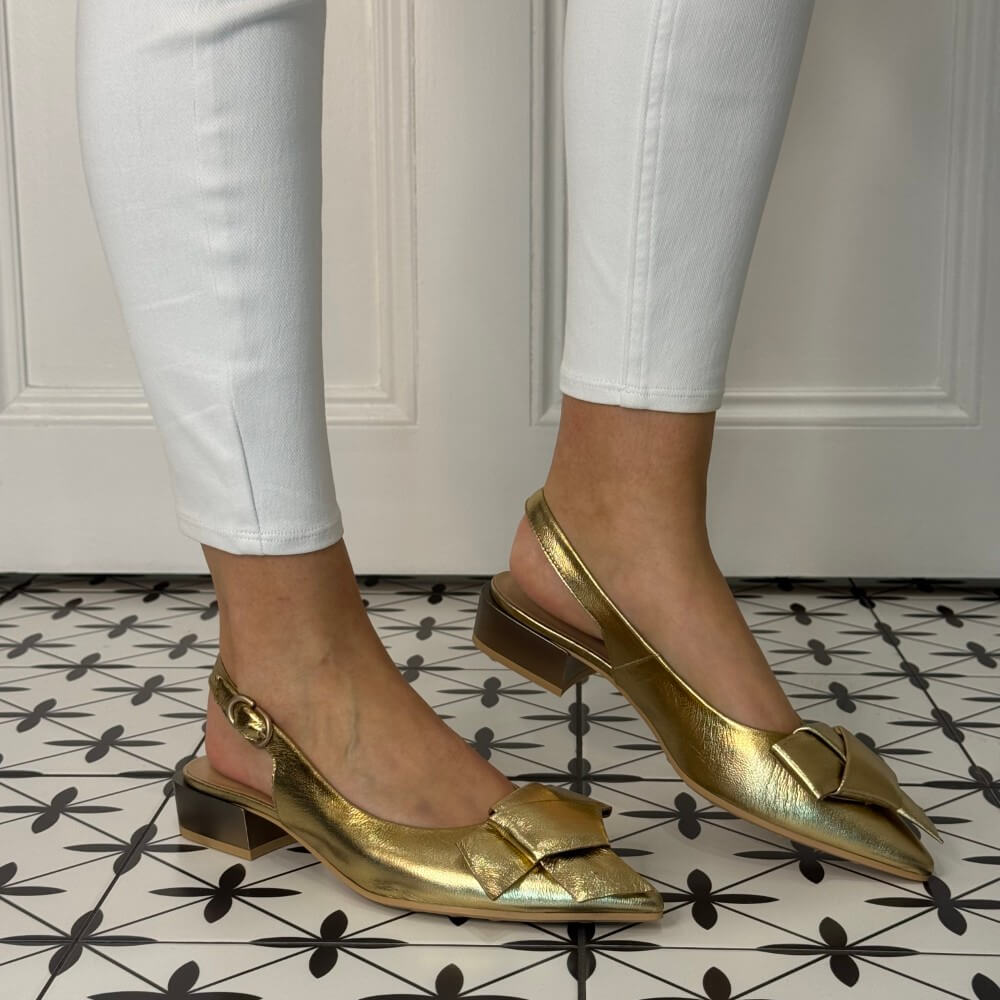 Hispanitas Platino Gold slingback shoes worn with white pants on a patterned floor.