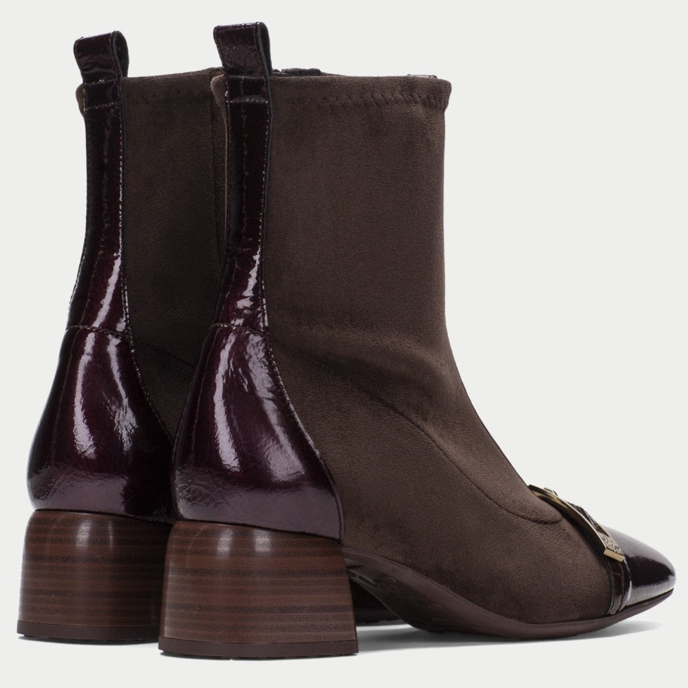 A pair of Hispanitas dark brown ankle boots with a mix of matte suede and glossy patent leather panels, featuring a stacked wood-look block heel and a small gold buckle detail on the toe.