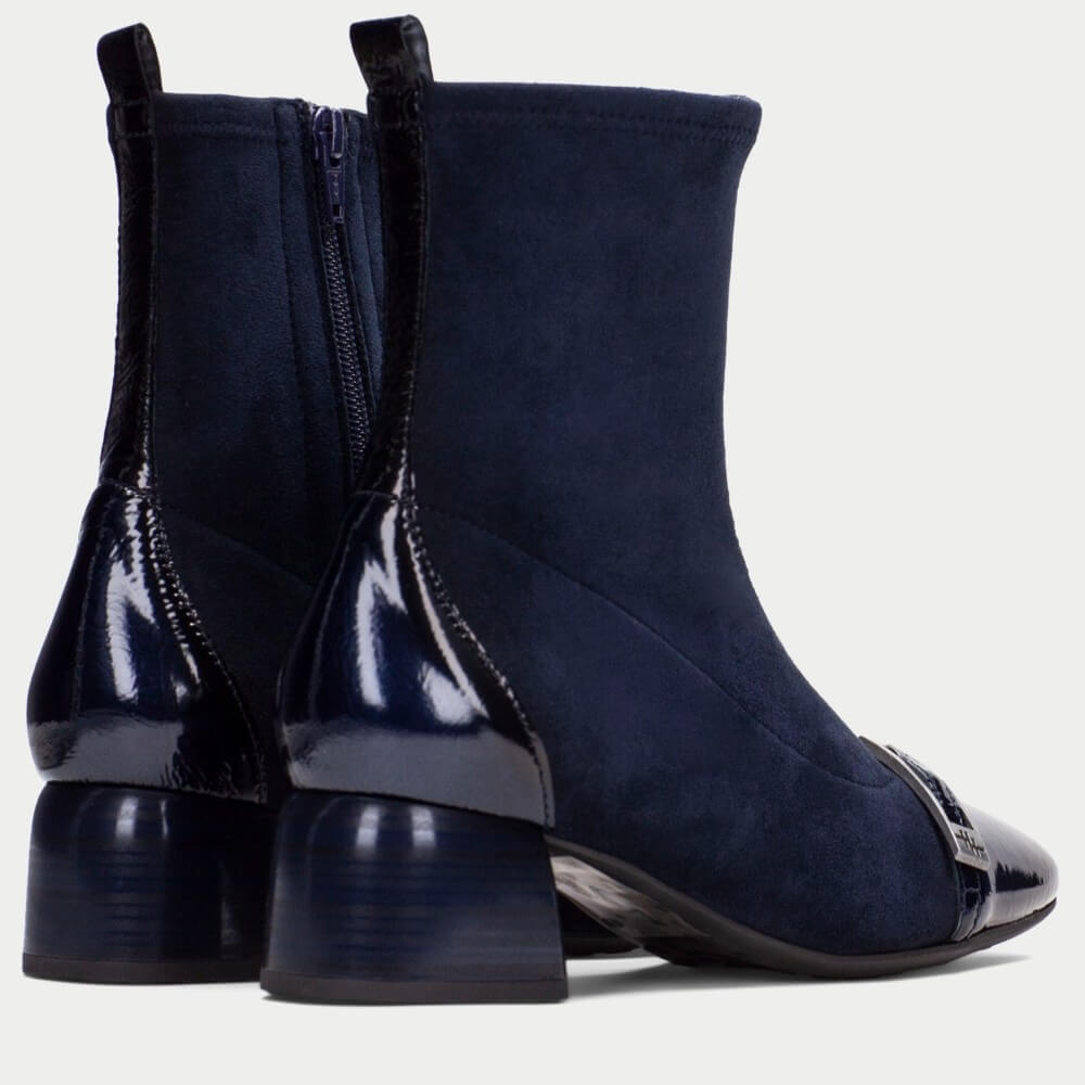 A pair of Hispanitas navy blue ankle boots with a mix of matte suede and glossy patent leather panels, featuring block heels and a pointed toe with a decorative strap detail, shown against a light gray background.