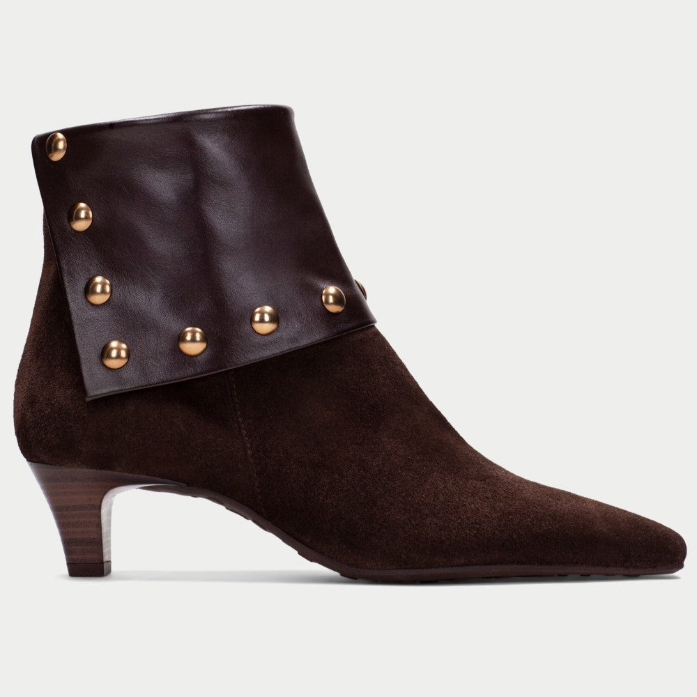 A Hispanitas dark brown suede and leather ankle boot with a pointed toe, a stacked wooden-look heel, and a wide leather cuff embellished with gold-tone studs, shown against a light grey background.