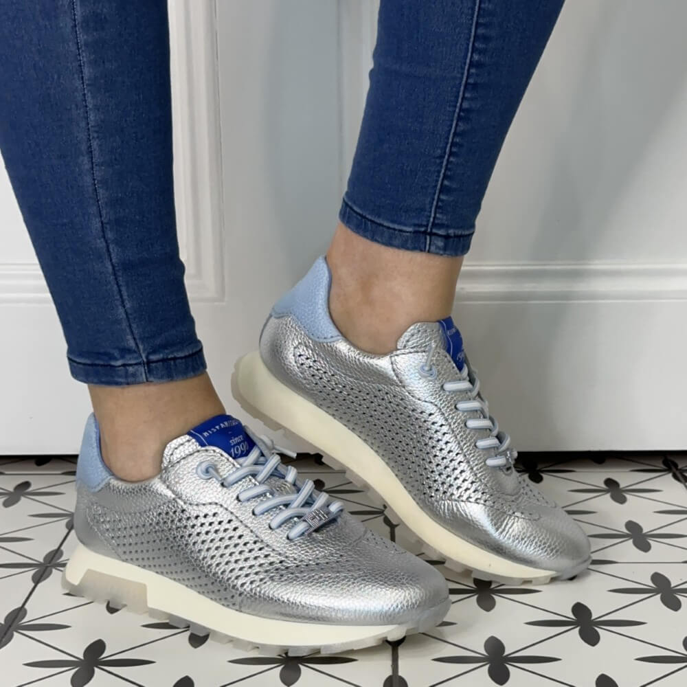 Silver sneakers with blue accents worn with blue jeans on a patterned floor.