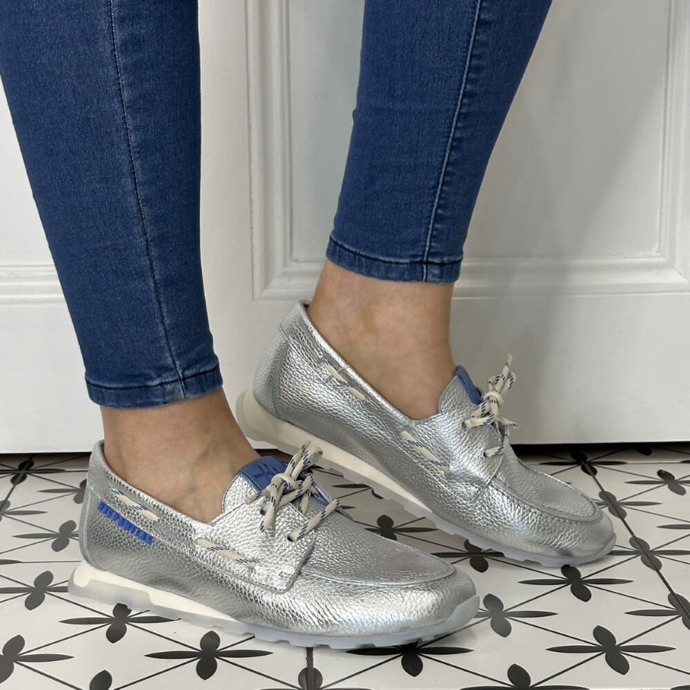 Silver loafers worn with blue jeans on a patterned floor.