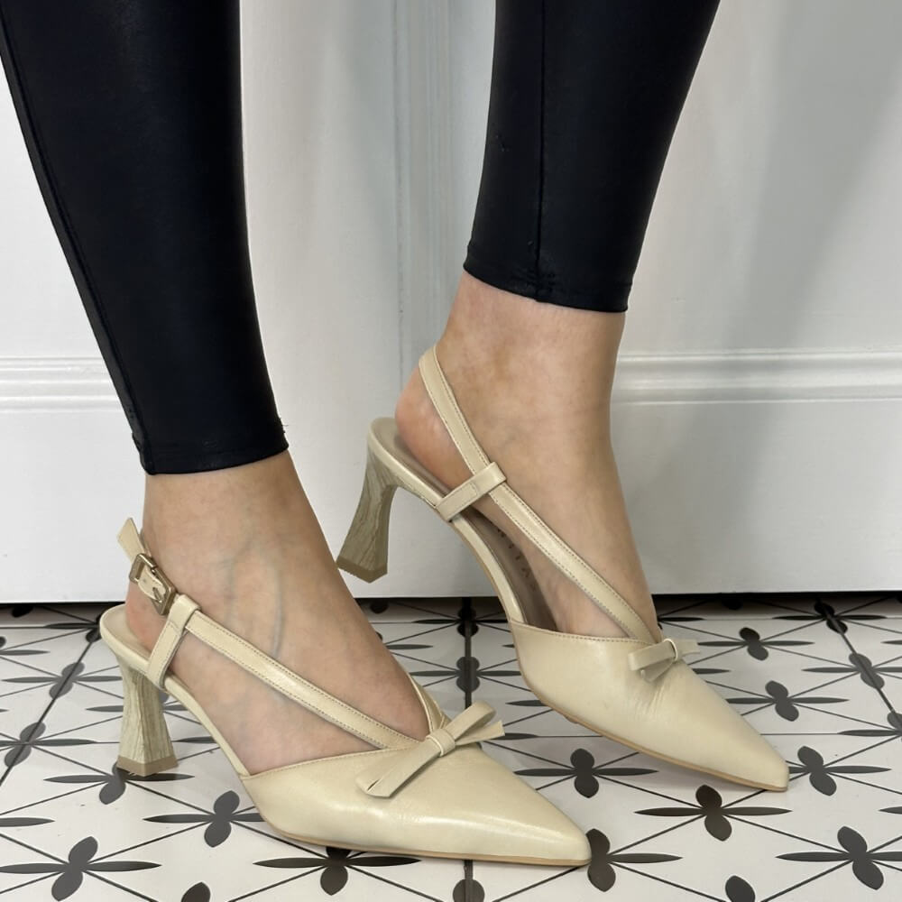 Beige high-heeled shoes worn with black pants on a patterned floor.