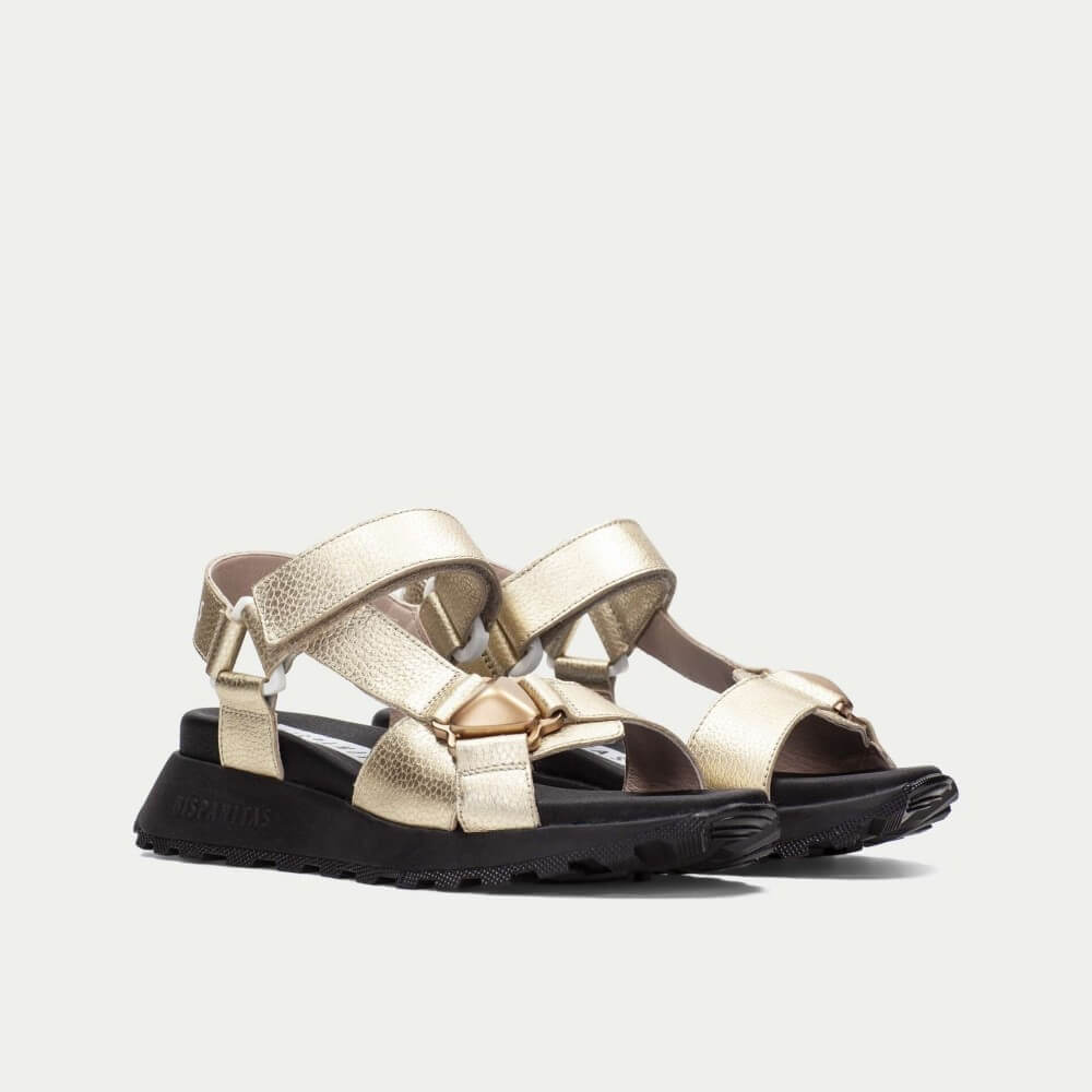 Gold sandals with black soles on a light gray background