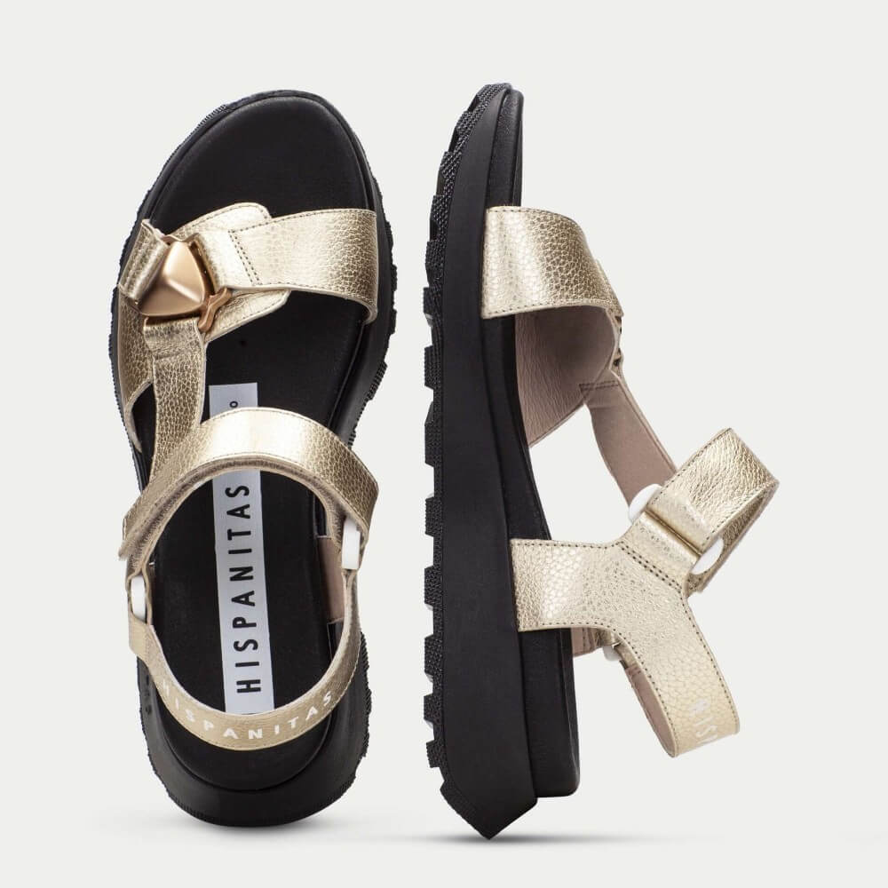 Gold sandals with black soles on a light gray background