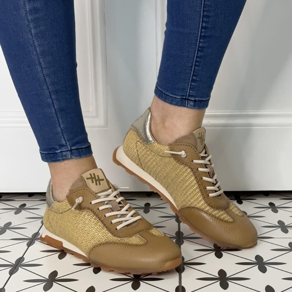 Beige sneakers worn with blue jeans on a patterned floor.