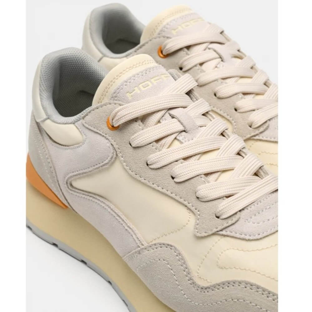 Pair of beige sneakers with orange accents on a light gray background