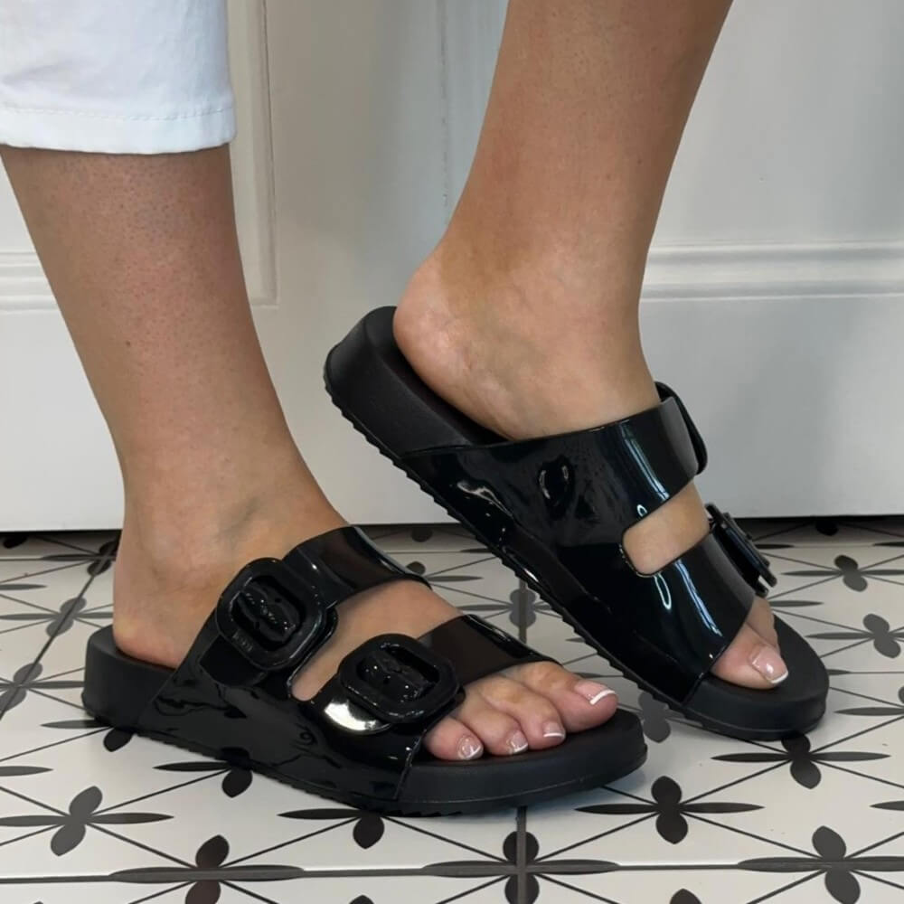 Igor Black patent leather sandals worn on a patterned floor.