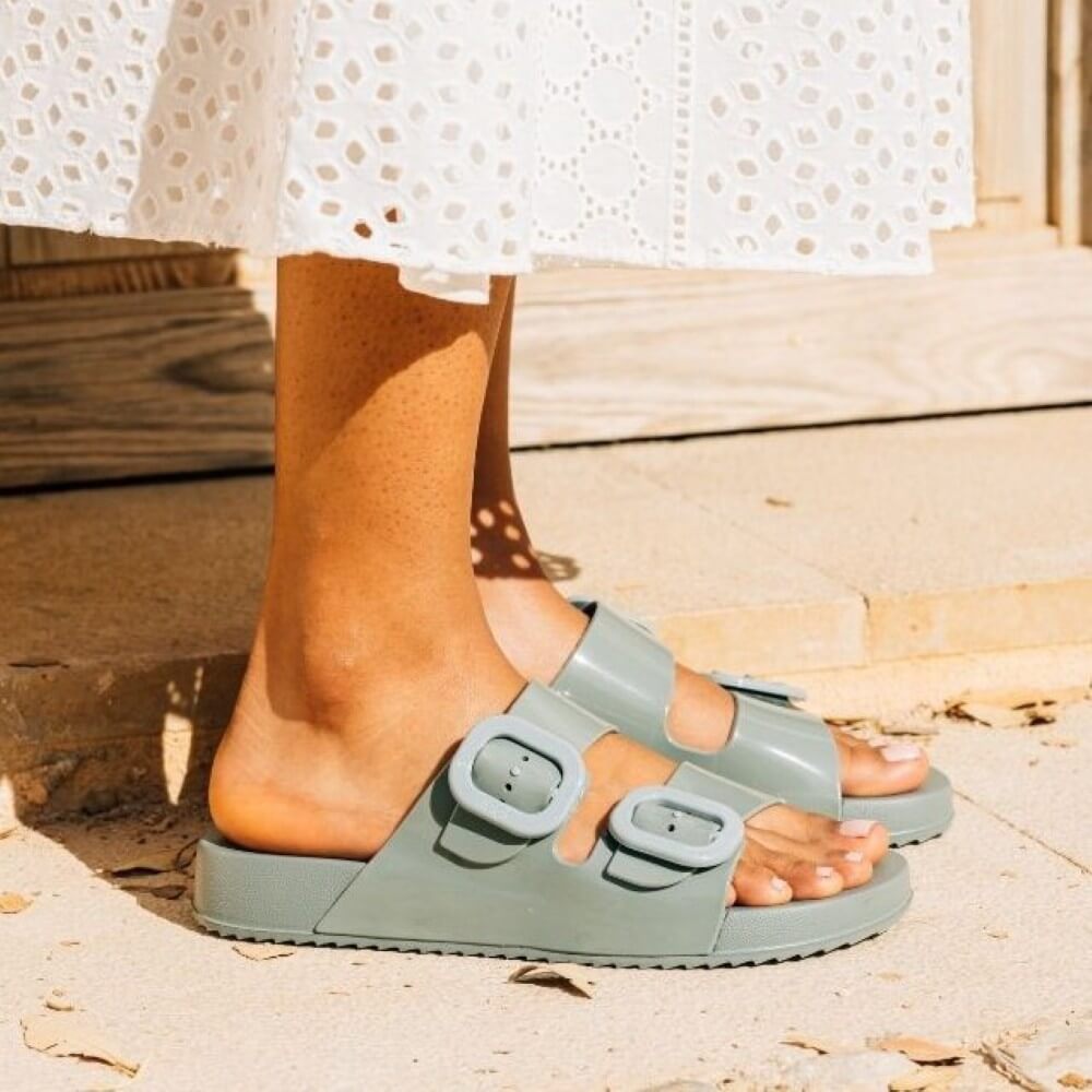 Person wearing light green sandals on a sandy surface with a blurred background