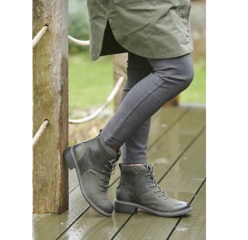 Person wearing green boots and pants standing on a wooden deck.