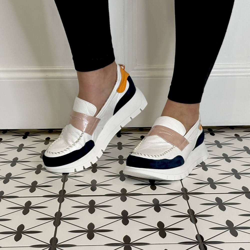 White sneakers with orange and navy accents worn by a person on a tiled floor.
