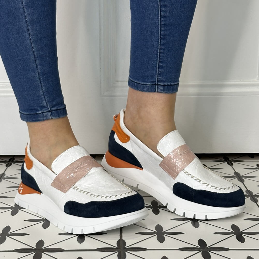 White sneakers with orange and navy accents worn by a person on a tiled floor.