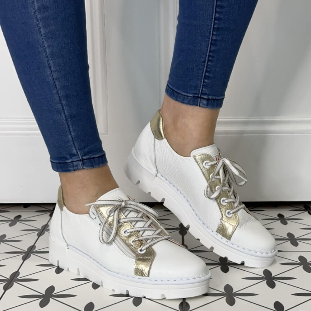 White sneakers with gold accents worn by a person on a tiled floor.