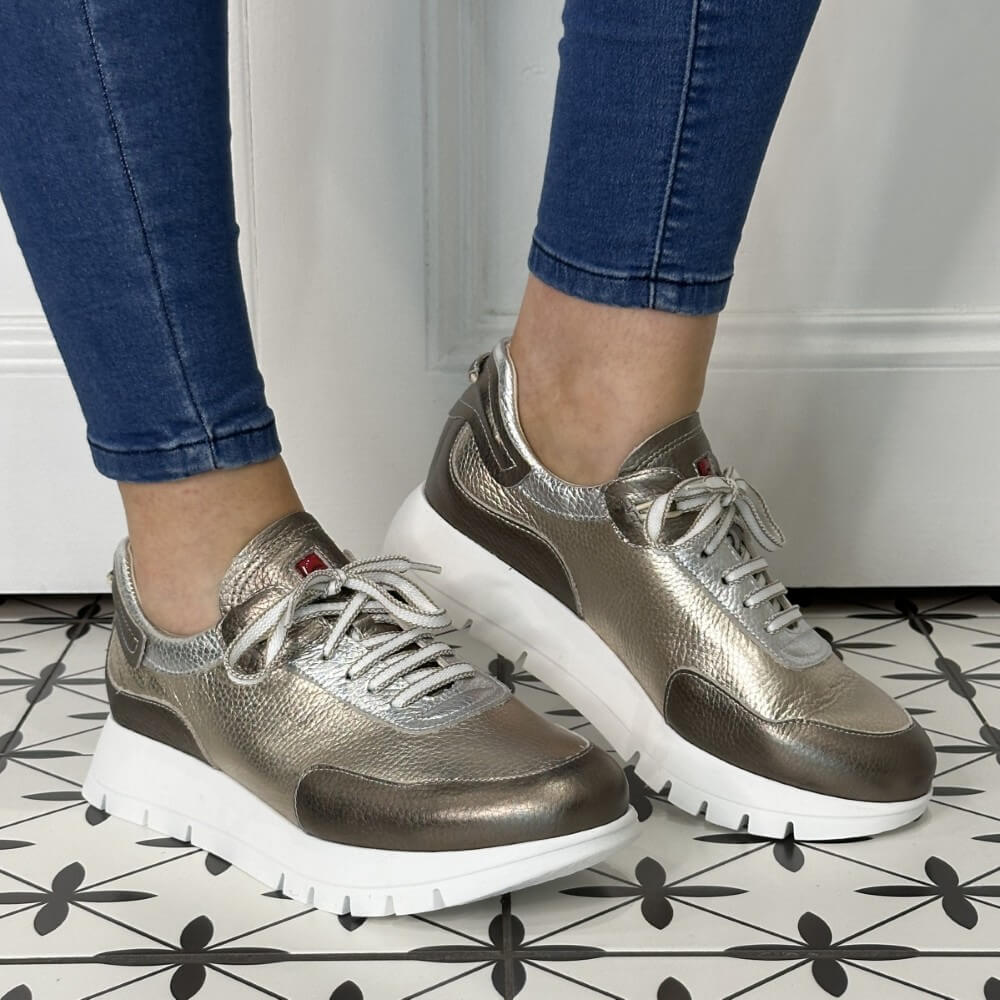 Gold, Silver and brown sneakers worn with blue jeans on a patterned floor.