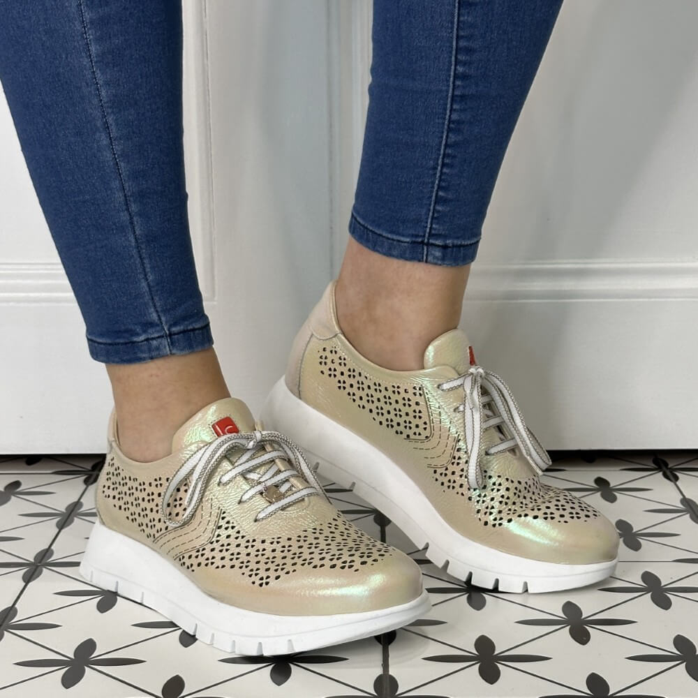 gold sneakers with laser cut details worn with blue jeans on a patterned floor.