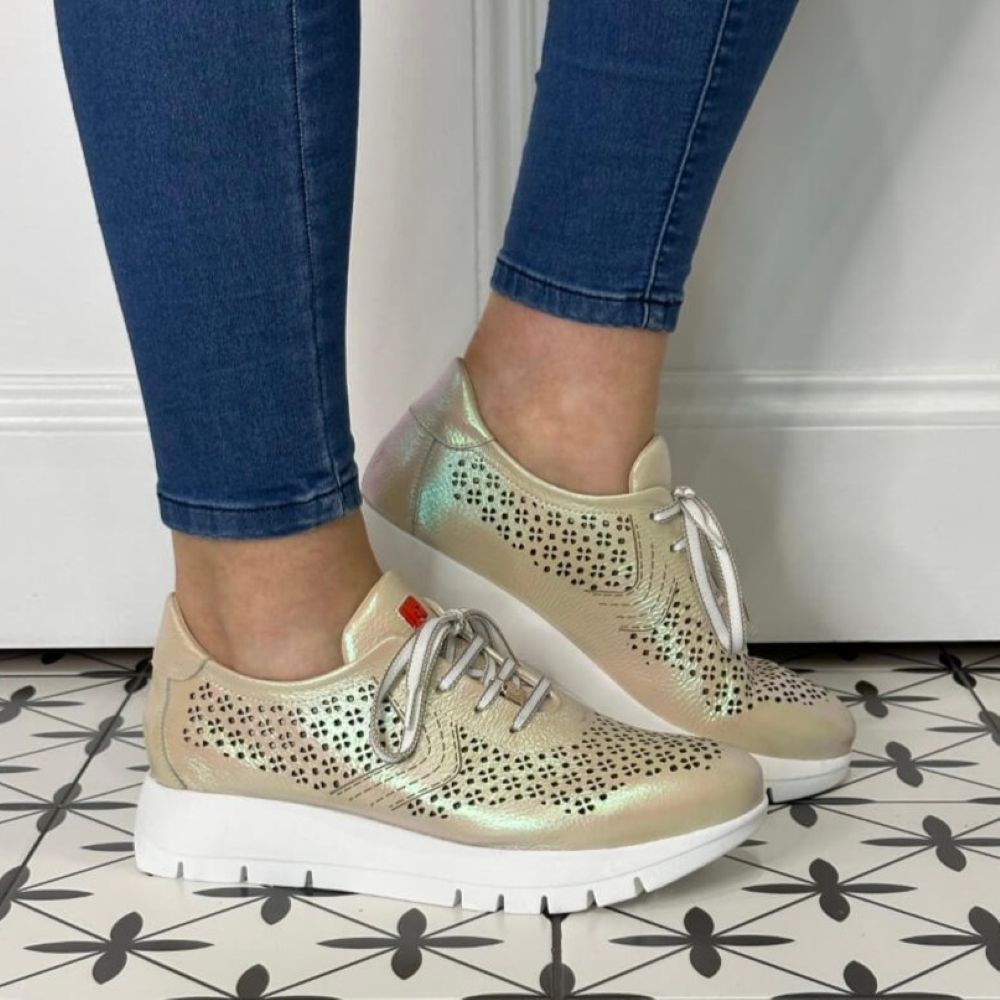 gold sneakers with laser cut details worn with blue jeans on a patterned floor.