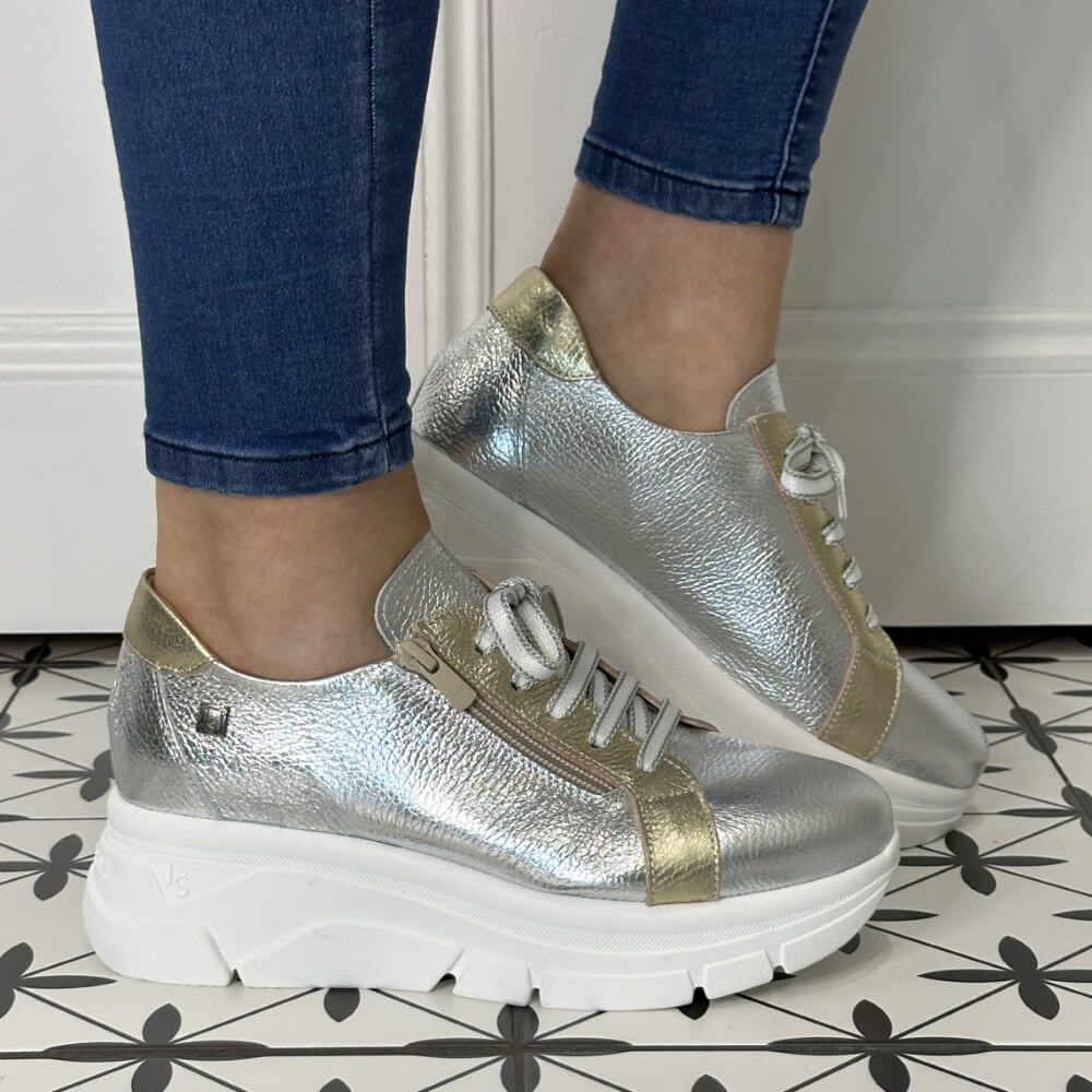 Silver and gold sneakers worn with blue jeans on a patterned floor.