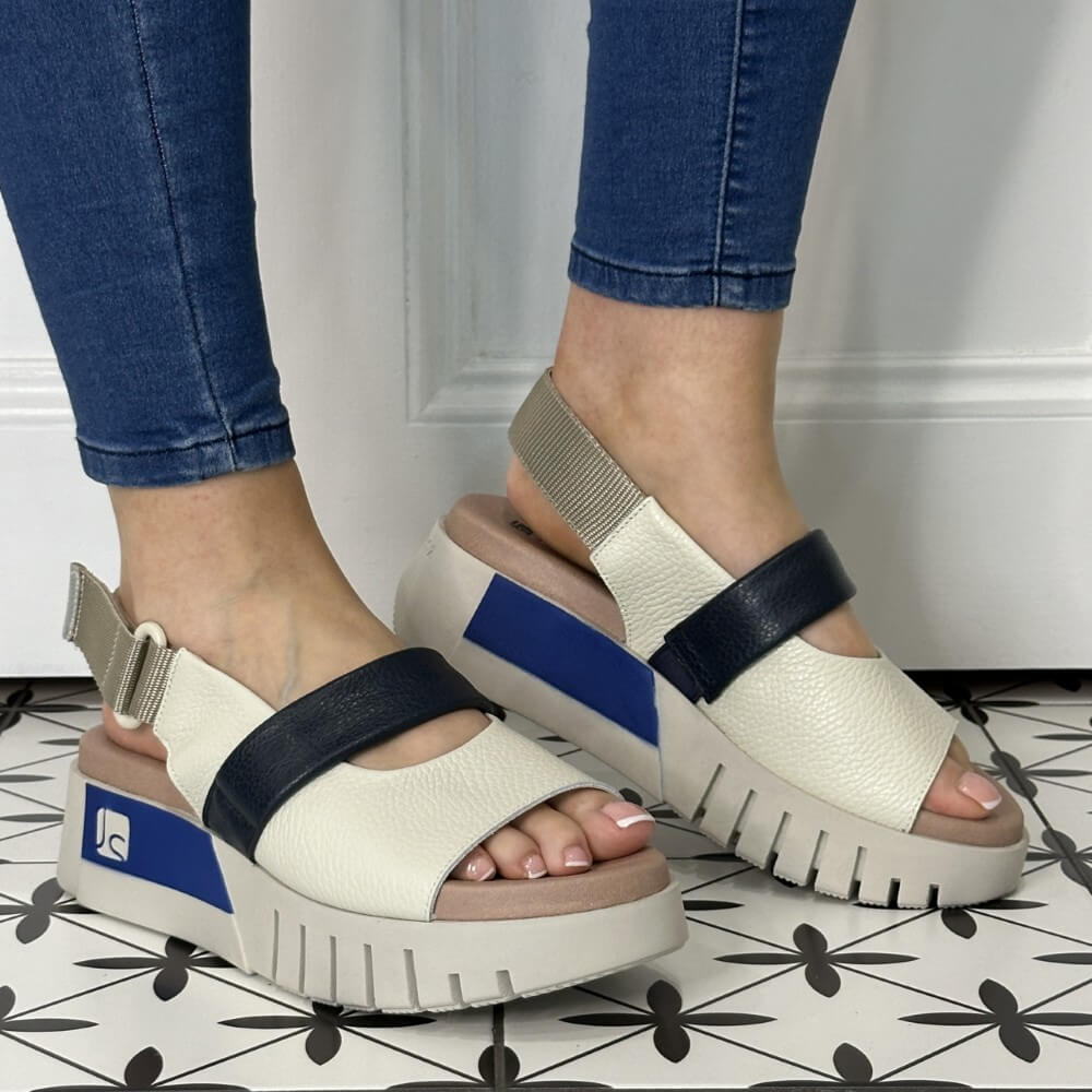 off White sandals with navy and blue straps worn by a person on a tiled floor.