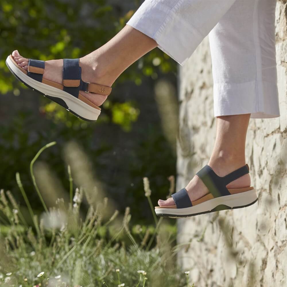 Person wearing Josef Seibel blue sandals with brown soles on a grassy and stone surface