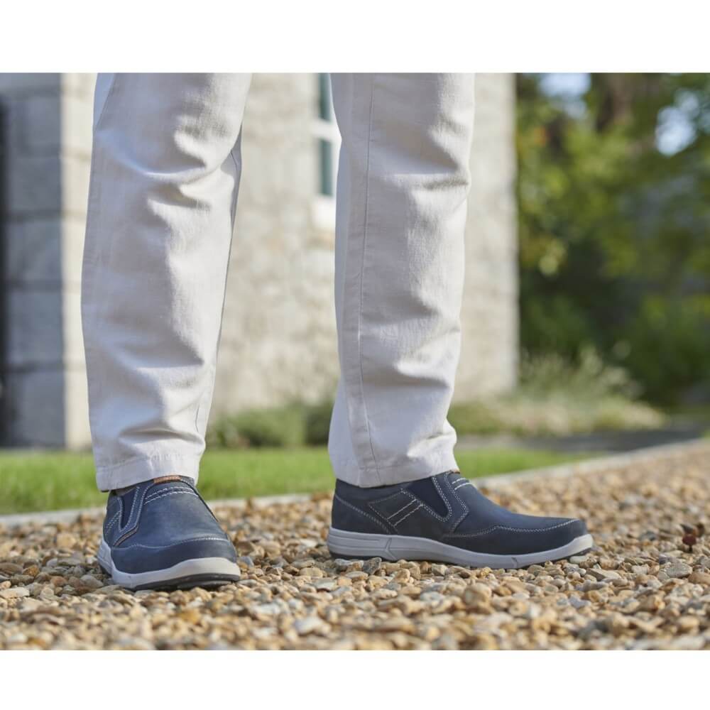 Person wearing Josef Seibel navy shoes and white pants standing on a gravel path with a blurred natural background