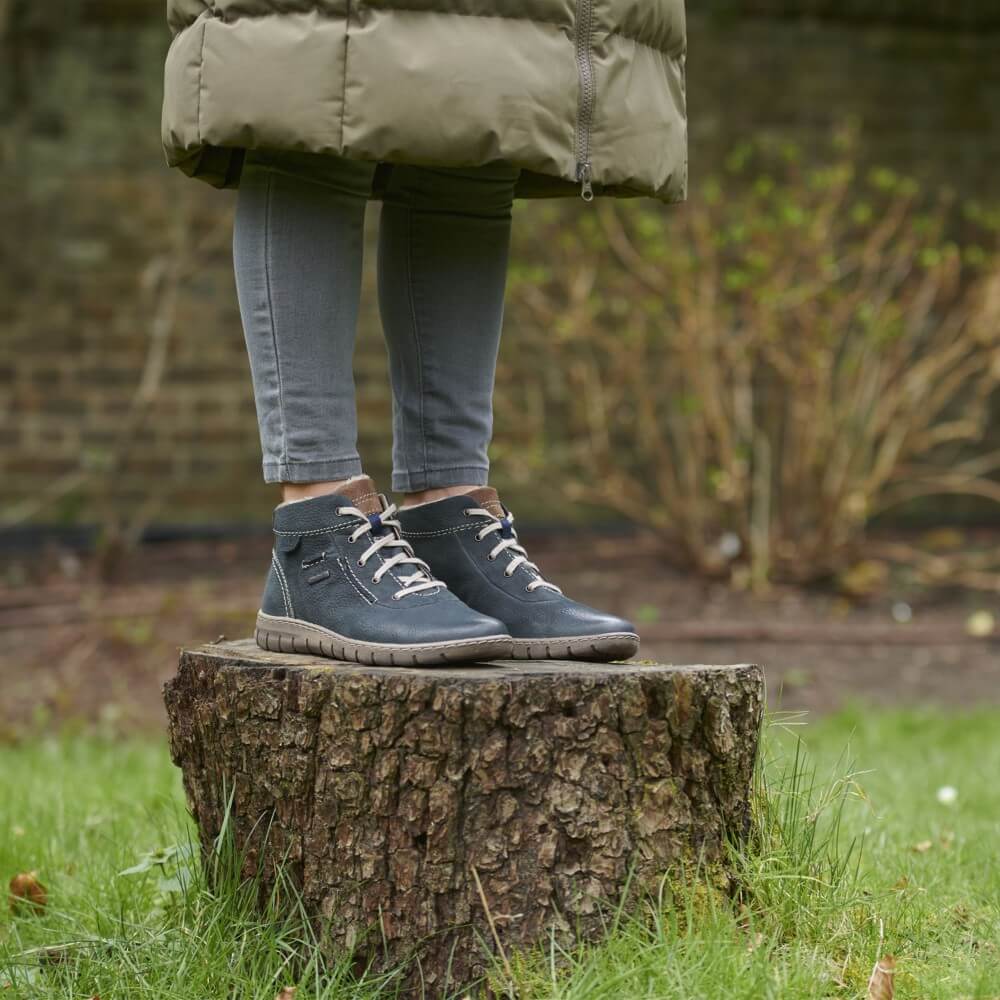 Person wearing dark blue boots standing on a tree stump in a garden setting