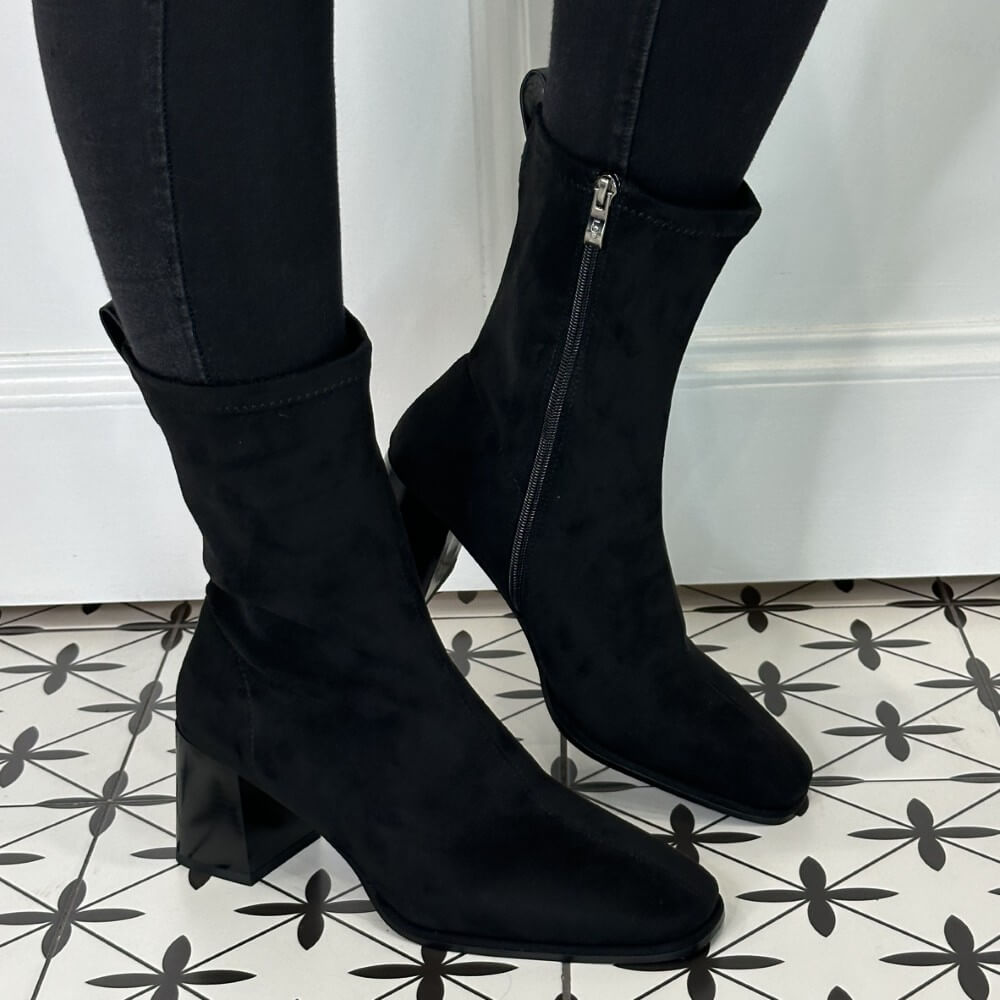 Black suede ankle boots worn with black pants on a patterned floor. Lodi A-Heka Ankle Boot