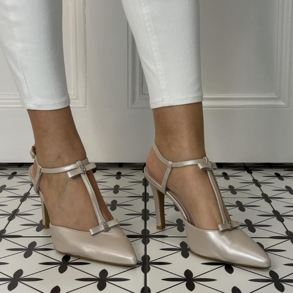 Silver high-heeled shoes worn with white pants on a patterned floor.