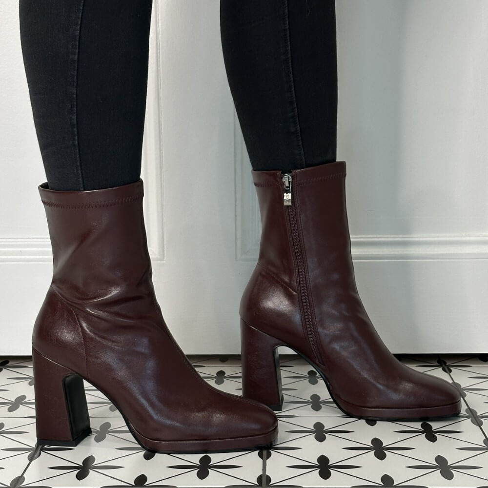 Burgundy boots worn with black pants on a patterned floor.