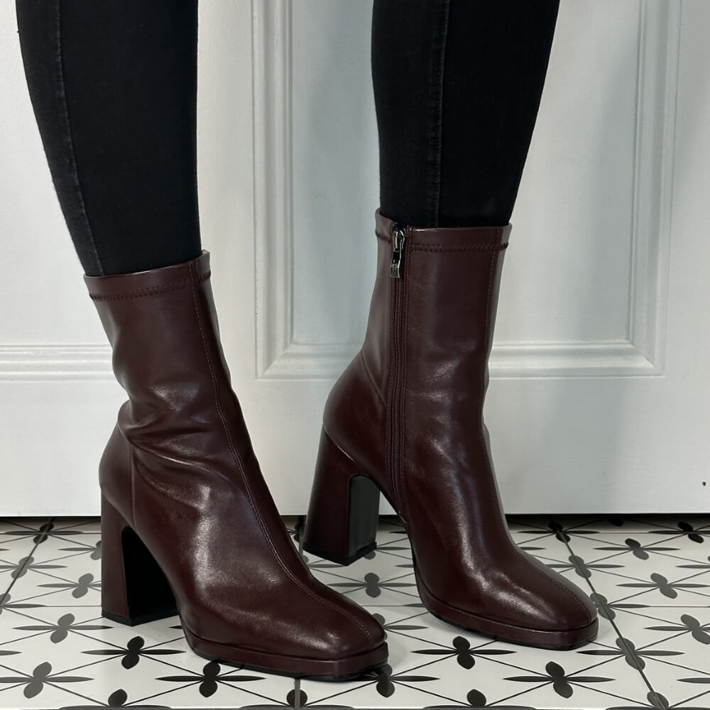 Burgundy boots worn with black pants on a patterned floor.
