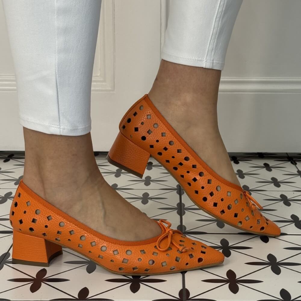 Orange perforated shoes worn with light blue jeans on a patterned floor.