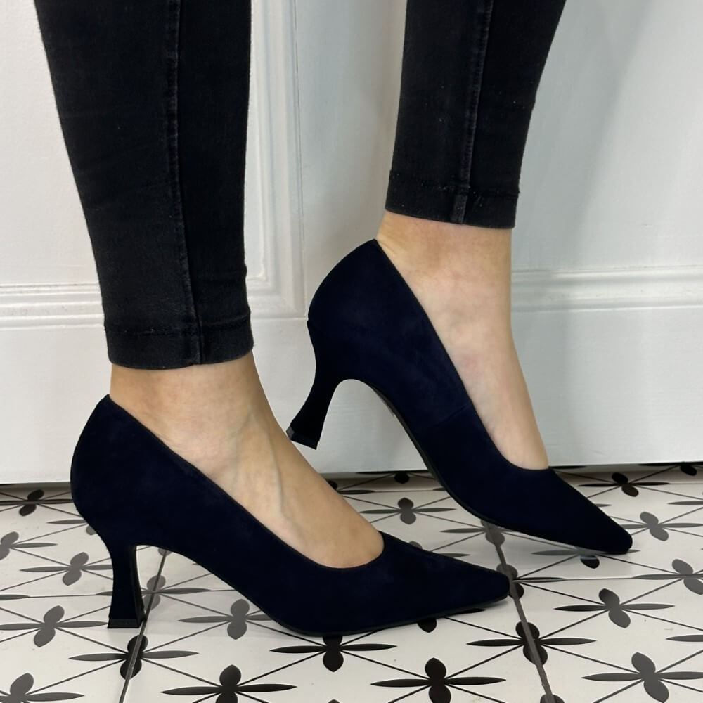 Navy blue high-heeled shoes worn with black pants on a patterned floor.