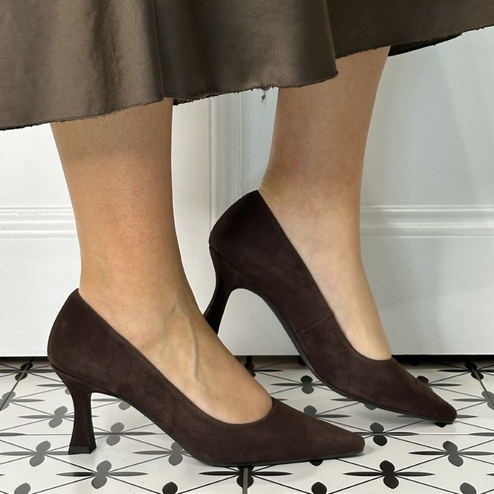 Brown high-heeled shoes worn with a skirt on a patterned floor.