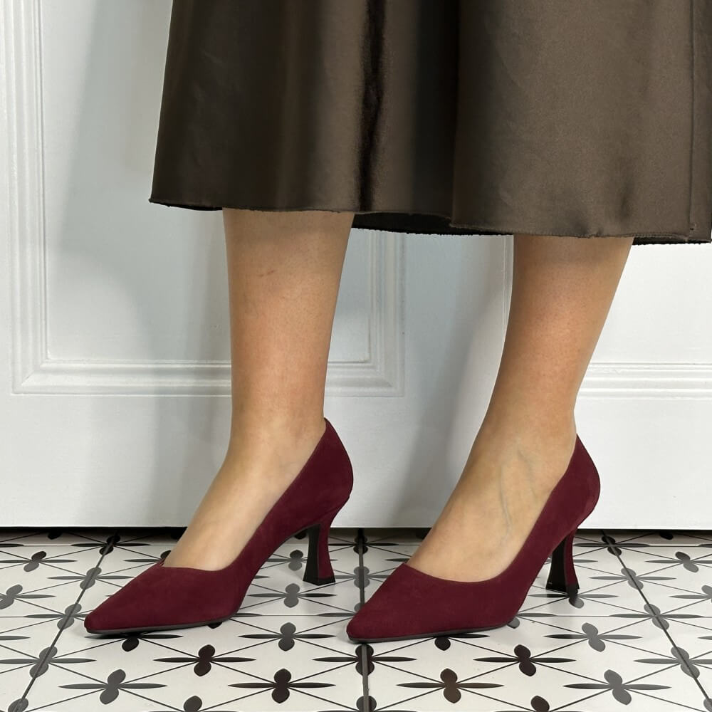 Burgandy suede high-heeled shoes worn by a person on a patterned