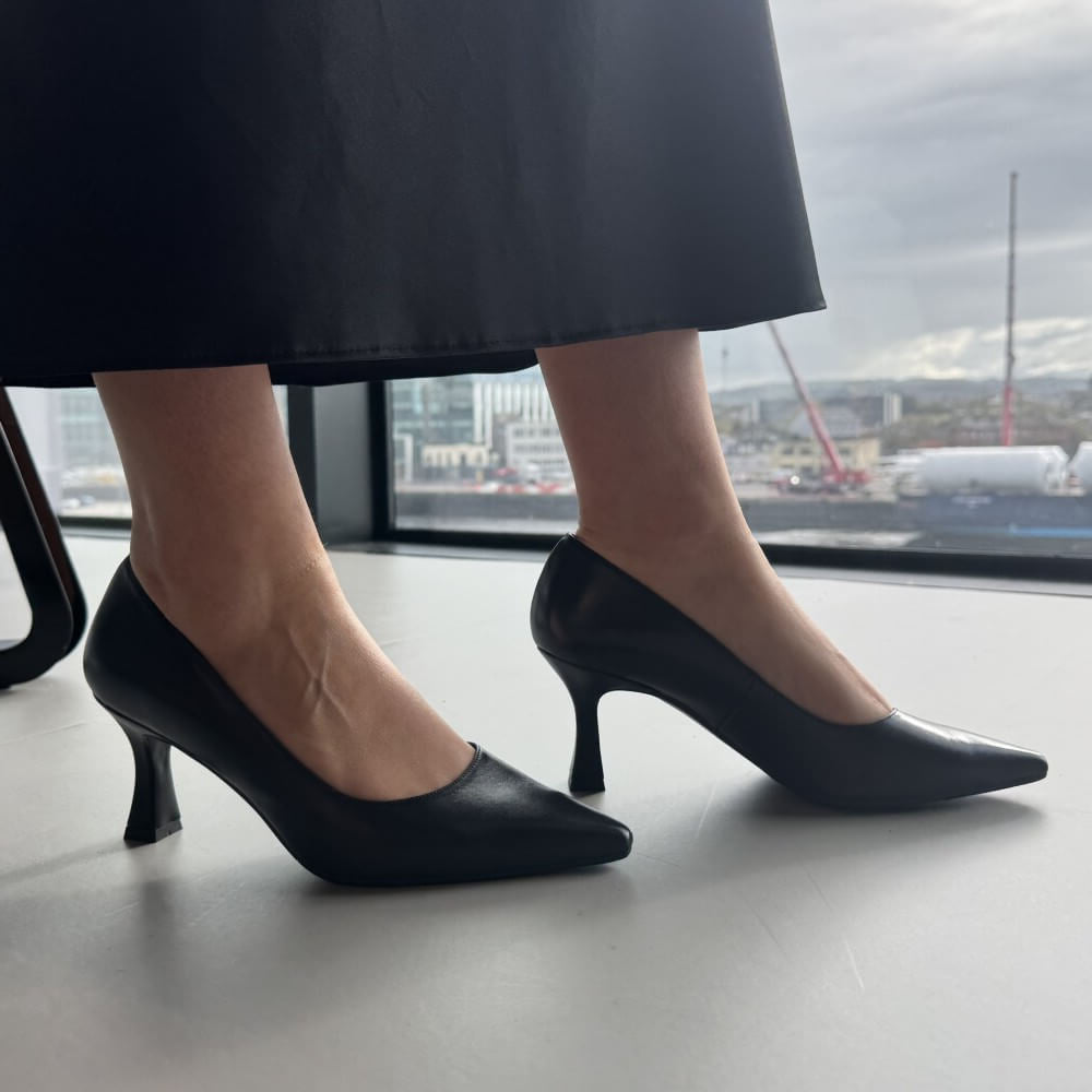 Black high-heeled shoes worn by a person standing indoors with a cityscape view.