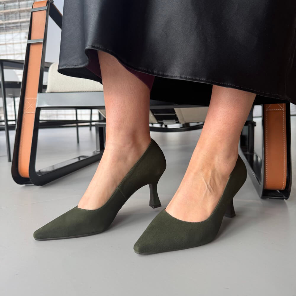 Green high-heeled shoes worn by a person sitting on a chair.