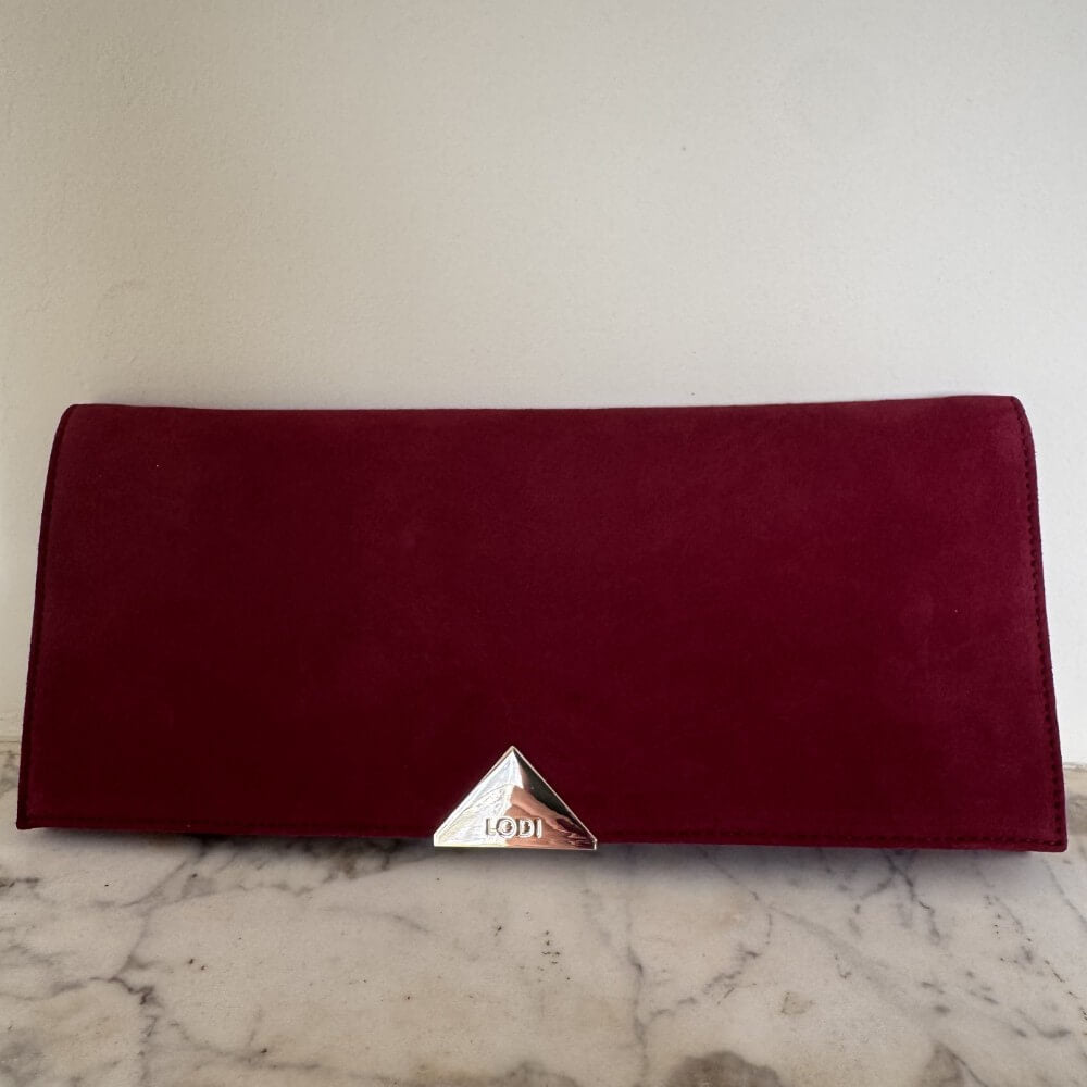 Burgundy Red Clutch with a gold Lodi emblem on a marble surface