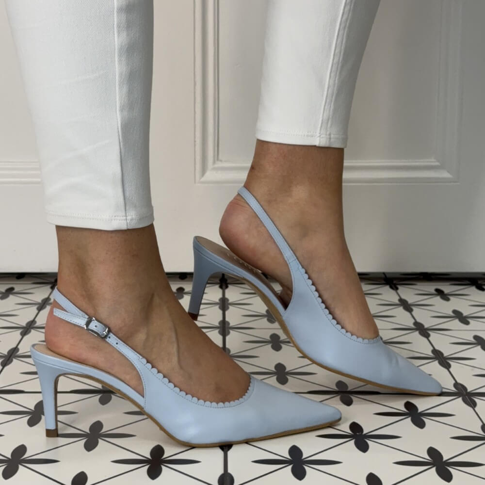 Light blue high-heeled shoes worn with white pants on a patterned floor.