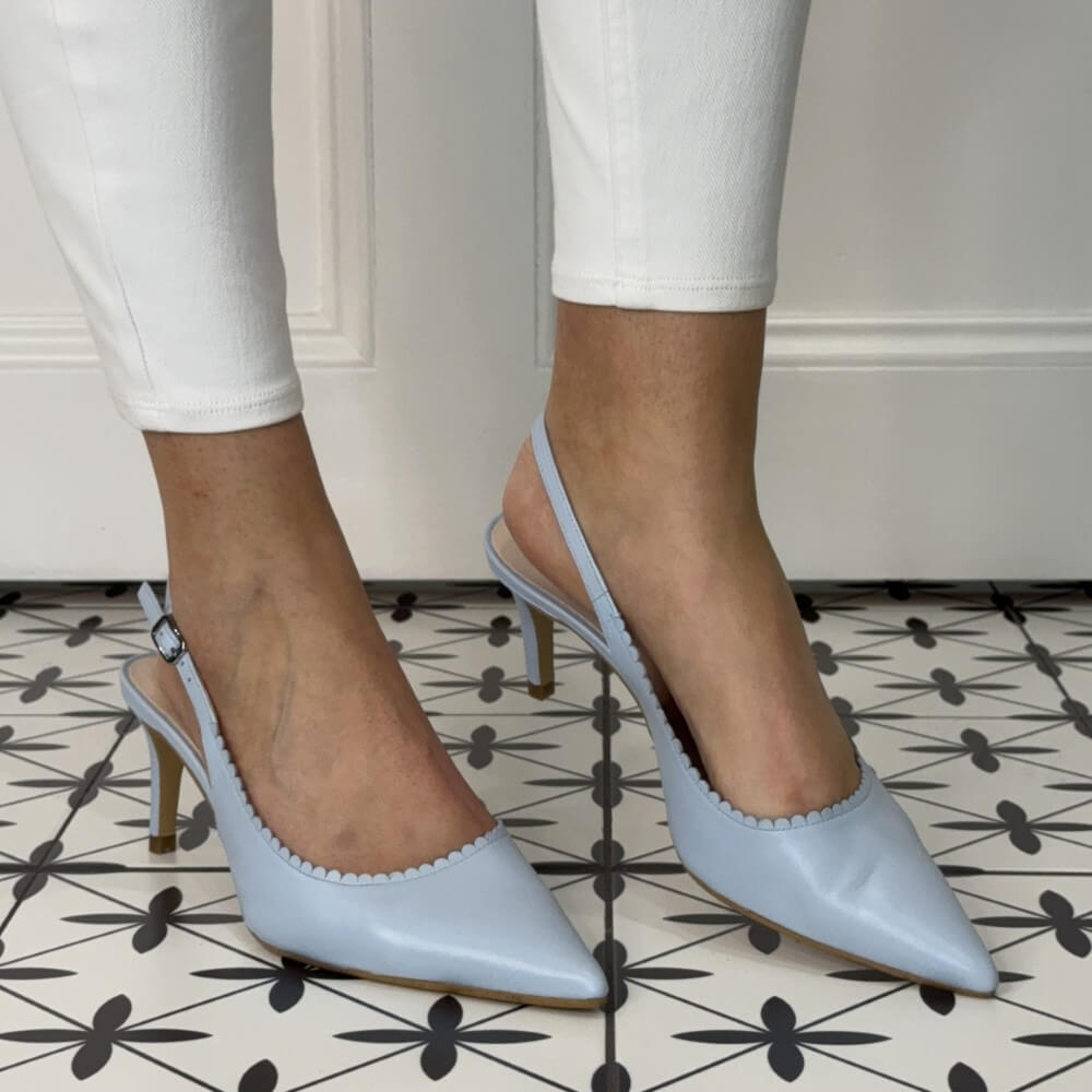 Light blue slingback heels worn with white pants on a patterned floor.