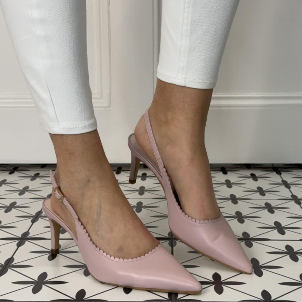 Pink high-heeled shoes worn with white pants on a patterned floor.
