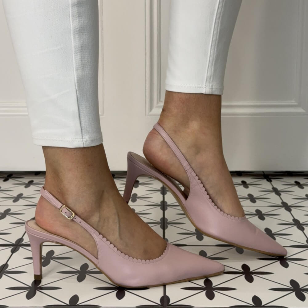 Pink high-heeled shoes worn with white pants on a patterned floor.