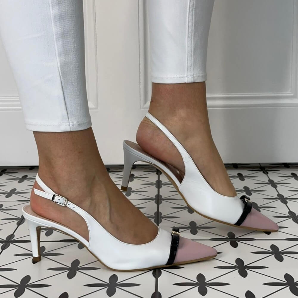 White high-heeled shoes with pink soles worn by a person on a patterned floor.