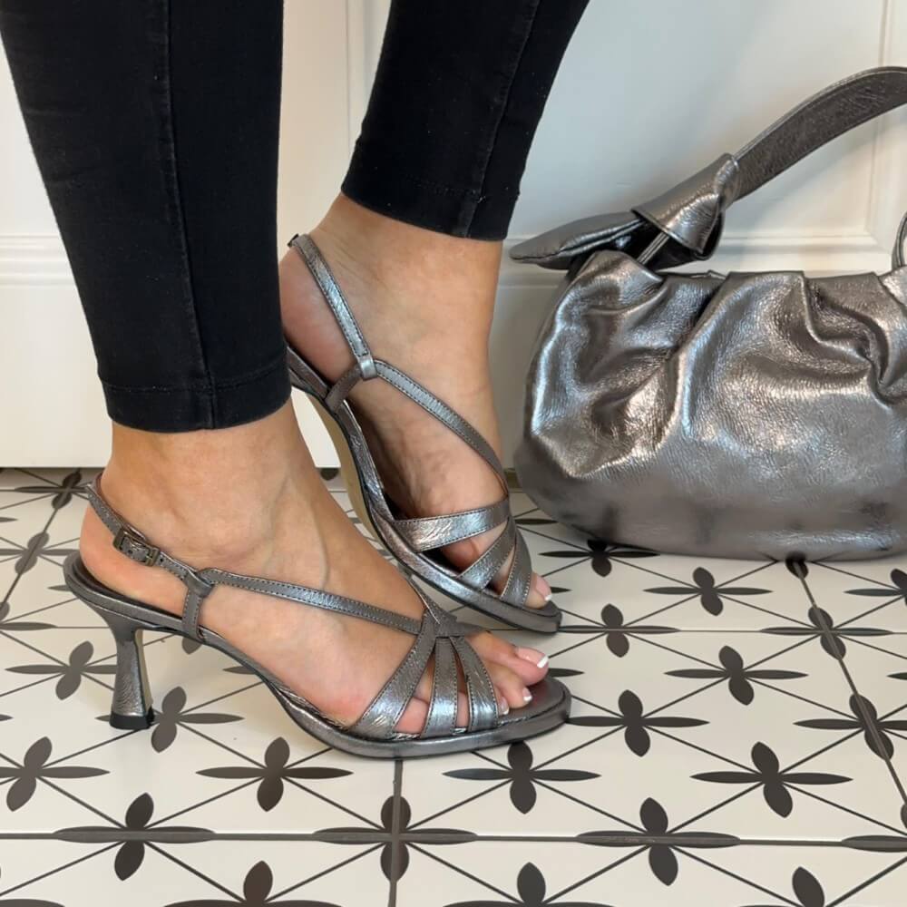 Dark Silver high-heeled sandals worn with black pants on a patterned floor, next to a matching Darksilver handbag. Marian 53305 Slingback Sandal Pewter Metallic