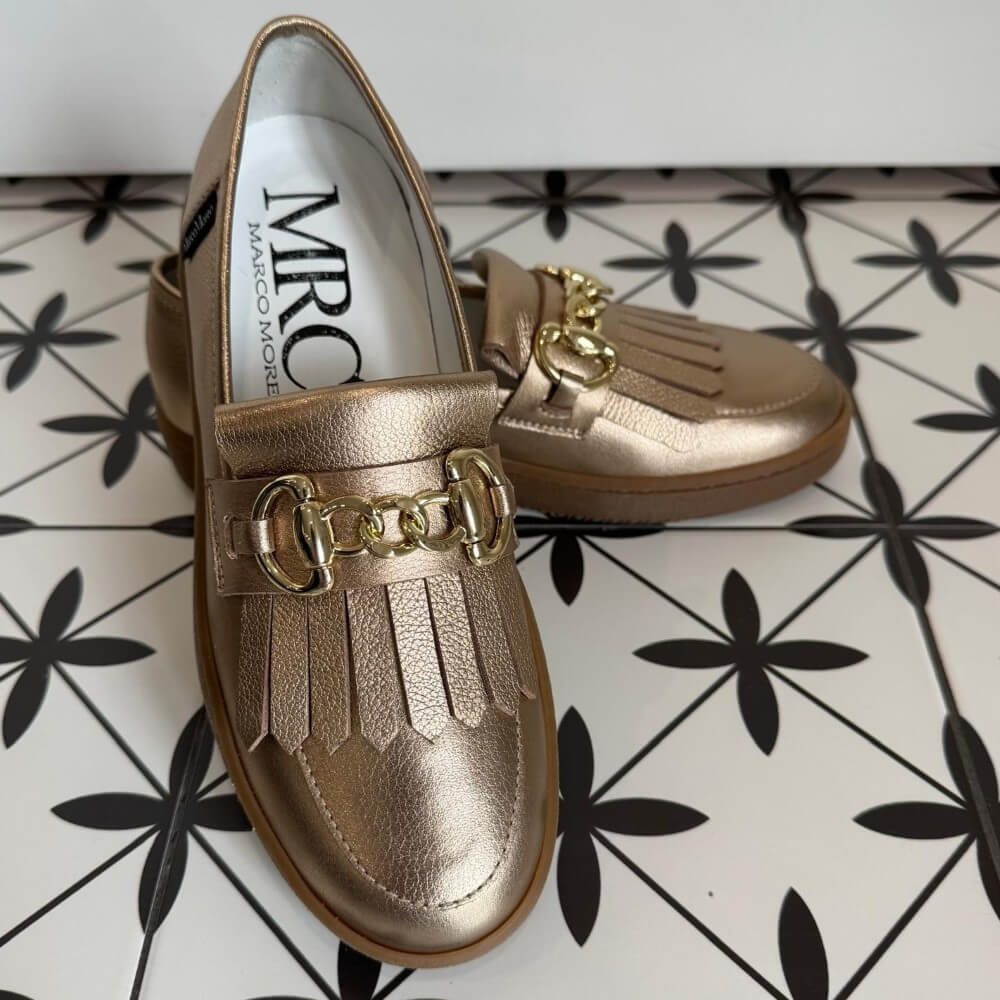 Pair of Marco Moreo gold bronze loafers with a gold buckle on a tiled floor. X760