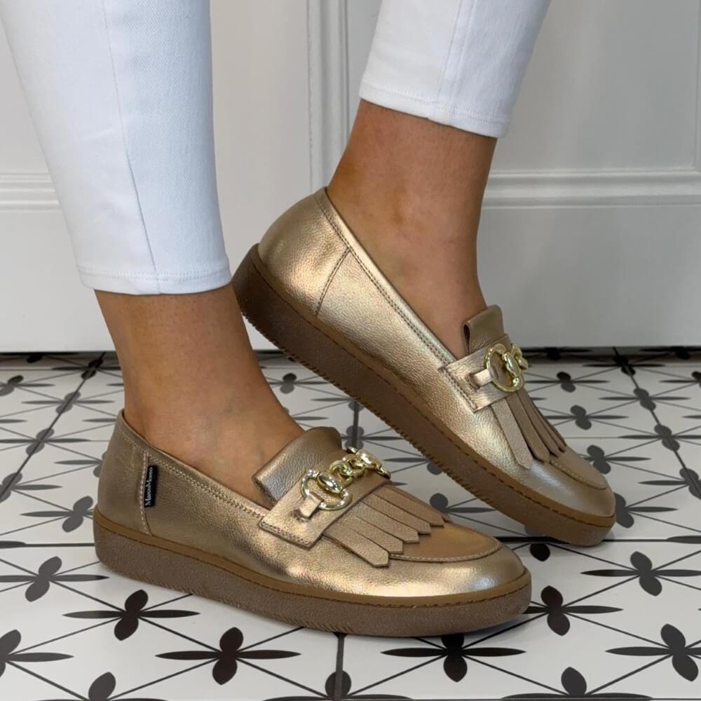 Marco Moreo Gold loafers with fringe details worn by a person on a patterned floor.