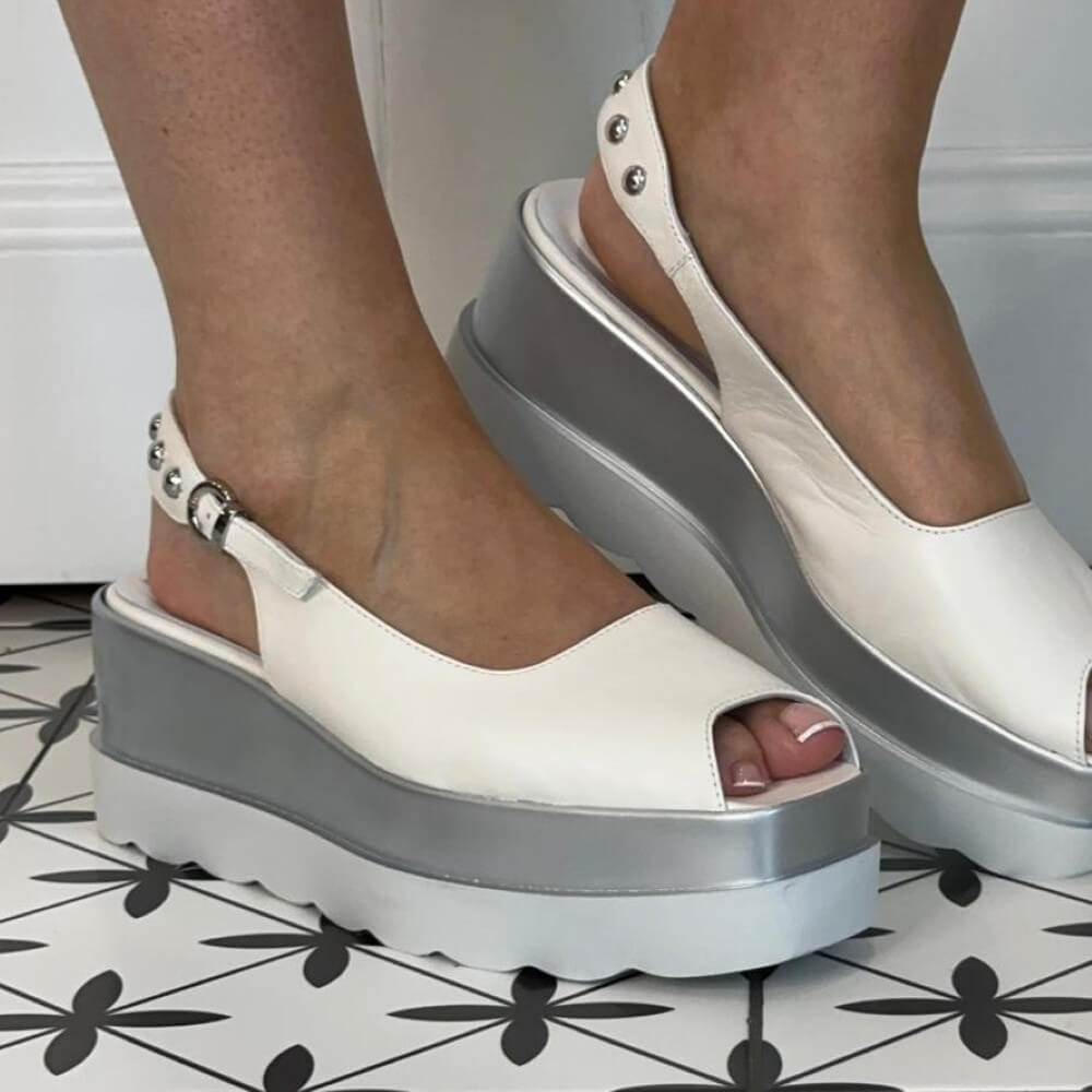Marco Moreo White and silver peep-toe sandals worn by a person on a black and white patterned floor.